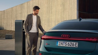 Woman in white top sitting in a Audi RS e-tron GT with black and red seats, viewed from outside through window.