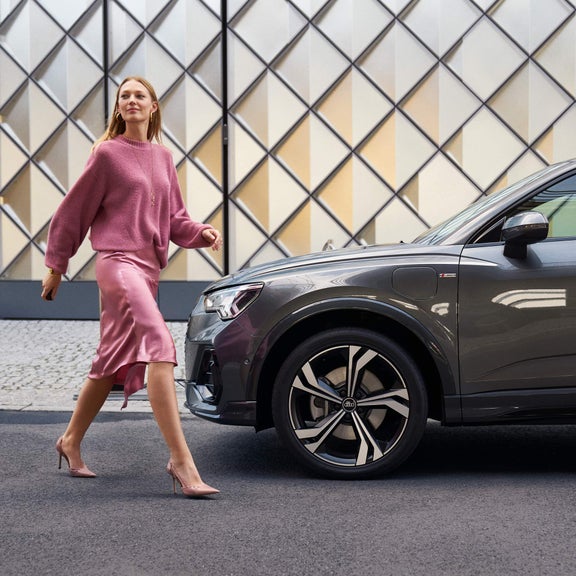 Lady in pink outfit looking over her shoulder walking towards Audi Q3.