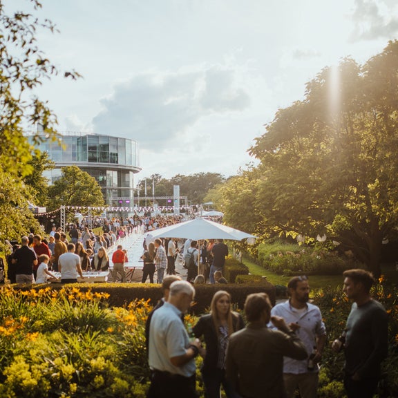 People stand in a park-like setting. The Audi museum mobile can be seen in the background.