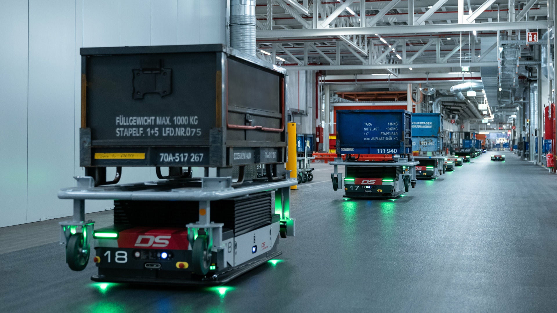 Fahrerlose Transportfahrzeuge fahren Kisten in einer langen Reihe durch eine Produktionshalle an ihren Einsatzort