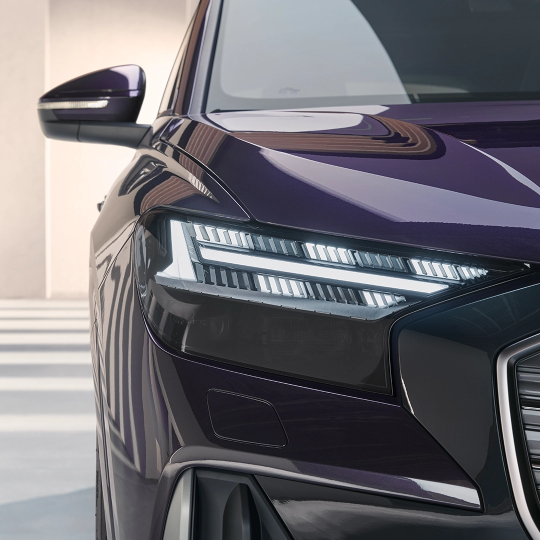 Dark purple Audi Q4 e-tron car, close-up of front left headlight and wing mirror, in a well-lit room.