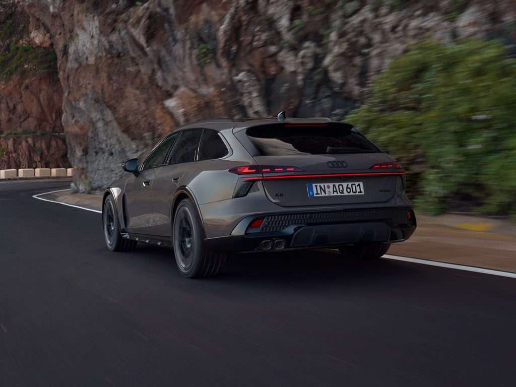 Der Audi A6 allroad e-hybrid schräg von hinten in voller Fahrt auf einer Gebirgsstraße. Rechts ragen steile Felswände auf.
