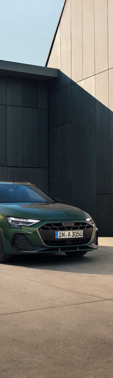 Grüner Audi A3 Sportback vor grauer Betonwand auf sonnigem Asphalt abgestellt.