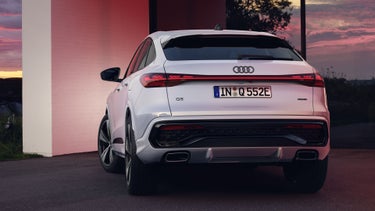 Heckansicht des Q5 Sportback e-hybrid, welcher vor bodentiefen Fenstern eines Hauses steht und diese mit seinen Scheinwerfern anleuchtet.