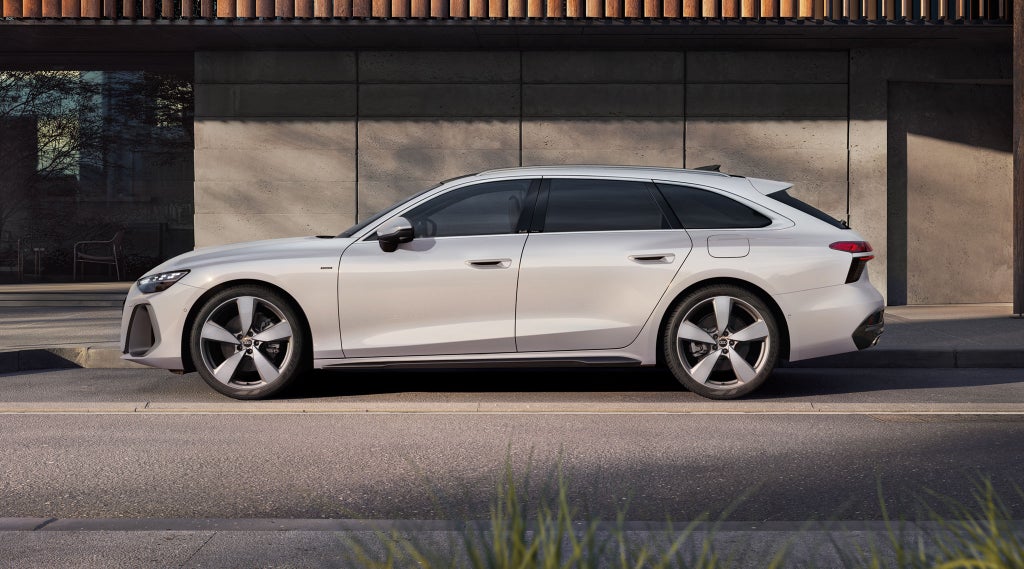 Der A6 Avant e-hybrid steht im Seitenprofil in einer Parkbucht vor der Fassade eines Gebäudes.