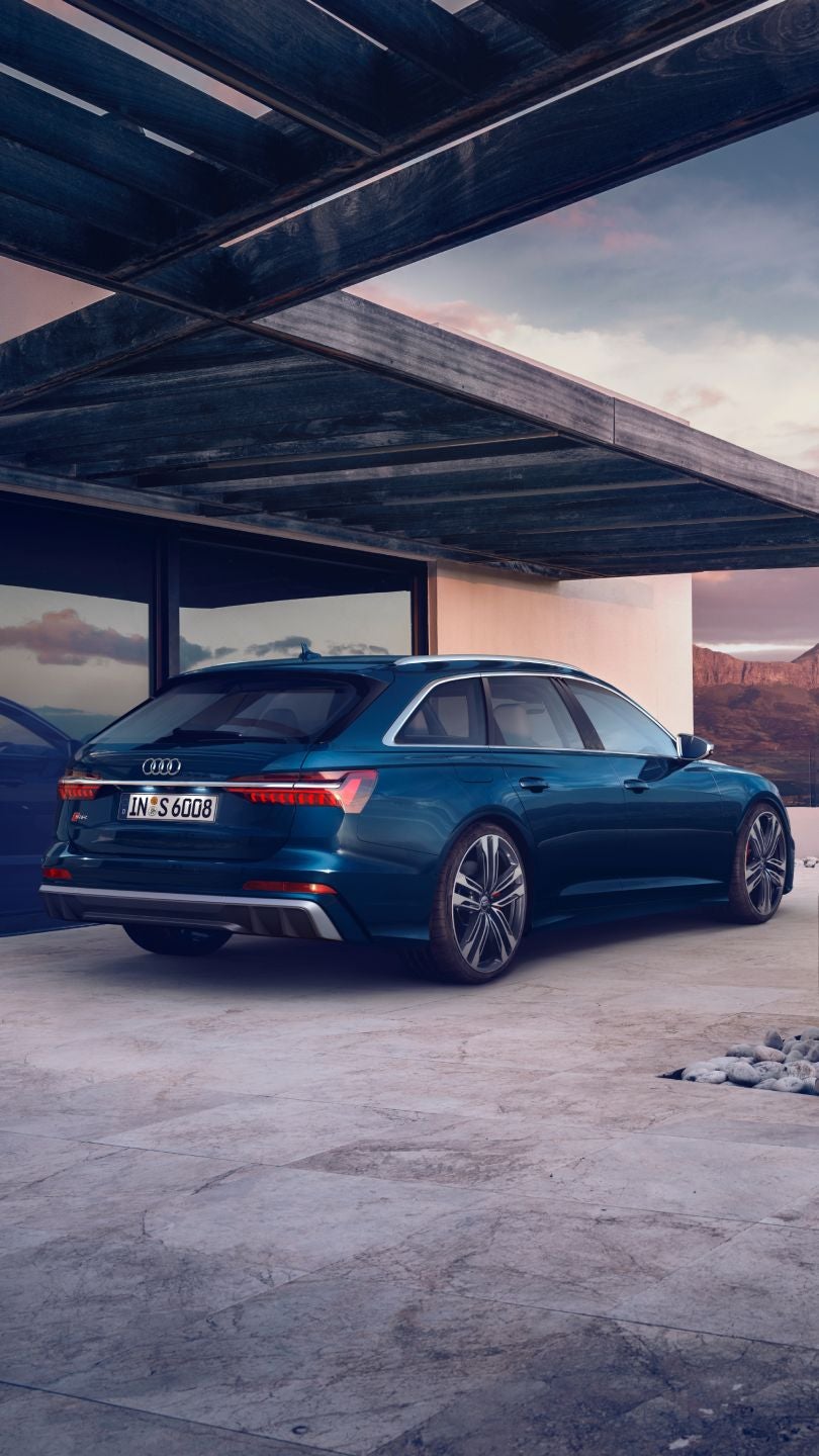 A blue Audi parked near a modern house with mountain views at dusk.