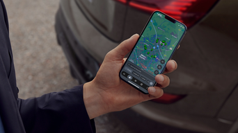 A hand holding a mobile phone with the myAudi app on screen displaying nearest charge stations