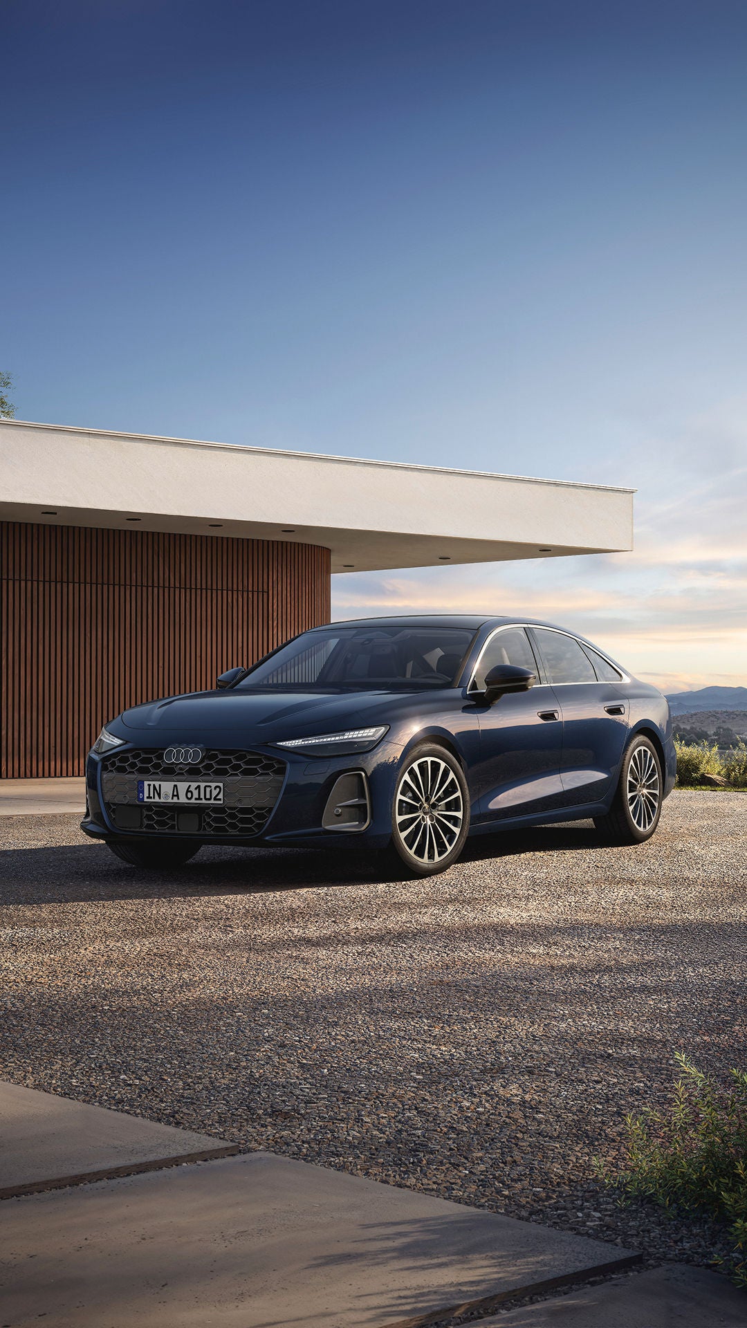 A sleek blue Audi sedan parked in front of a modern home, with mountains and a clear sky in the background.