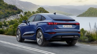 Seitliche Heckaufnahme des SQ6 Sportback e-tron in dunkelblau, welcher eine Straße in der Natur neben einem See entlangfährt.&nbsp;