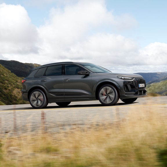 Seitliche Aufnahme des SQ6 SUV e-tron, welcher über eine Straße in einer bergigen Region fährt.