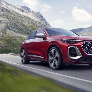 Schräges, vorderes Seitenprofil des roten SQ5 Sportback, welcher auf einer Straße durch die Berge fährt.