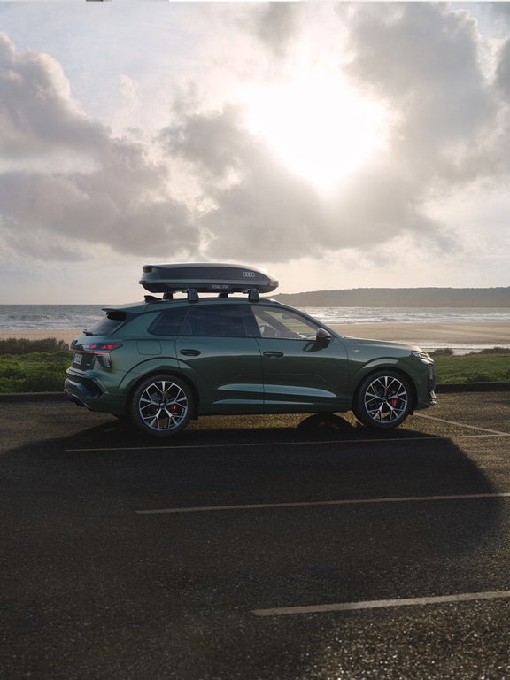 Side view of Audi Q3 SUV with roof box parking.