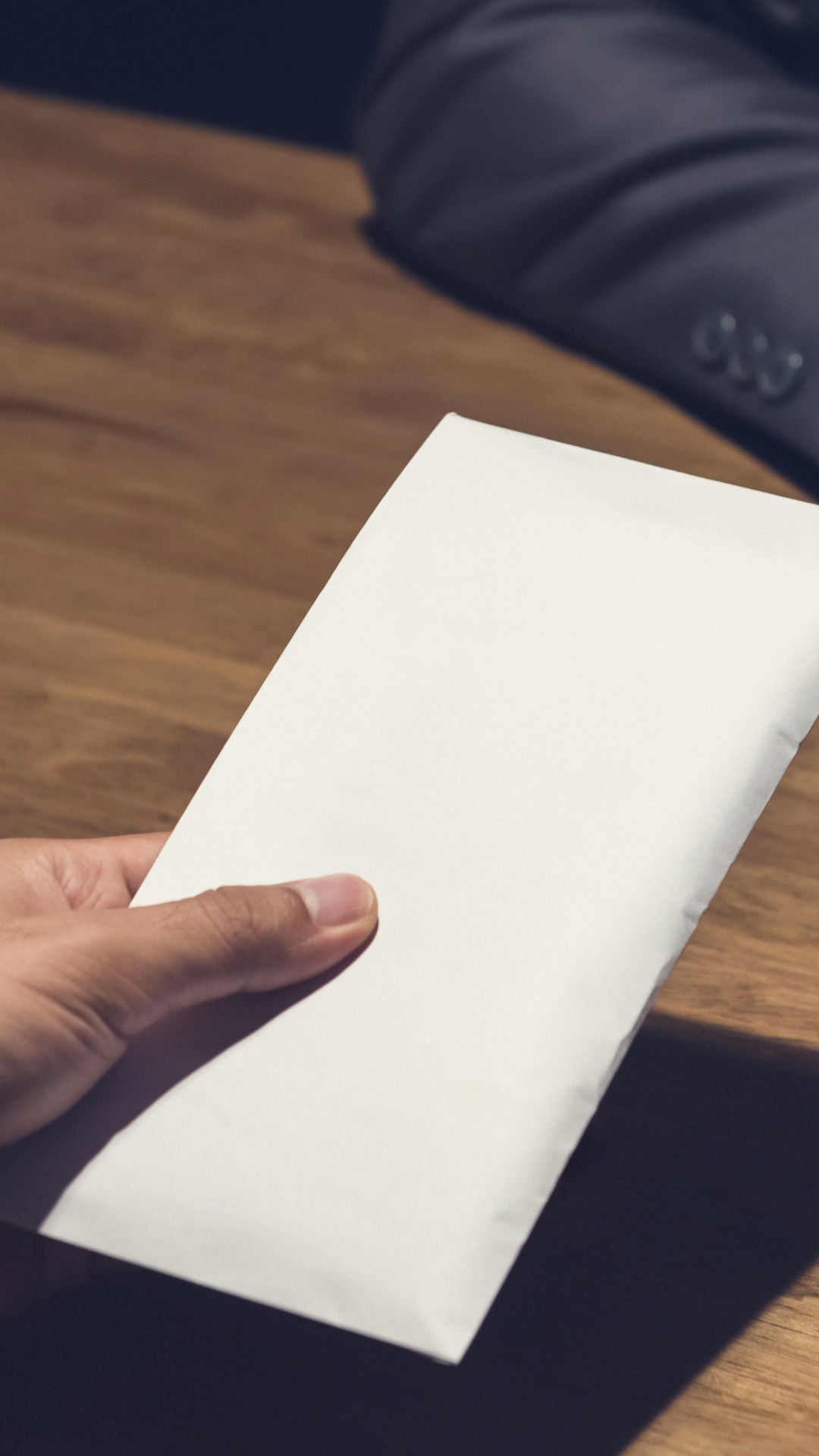 A hand passes an envelope across the table, the other person raises a hand in refusal.