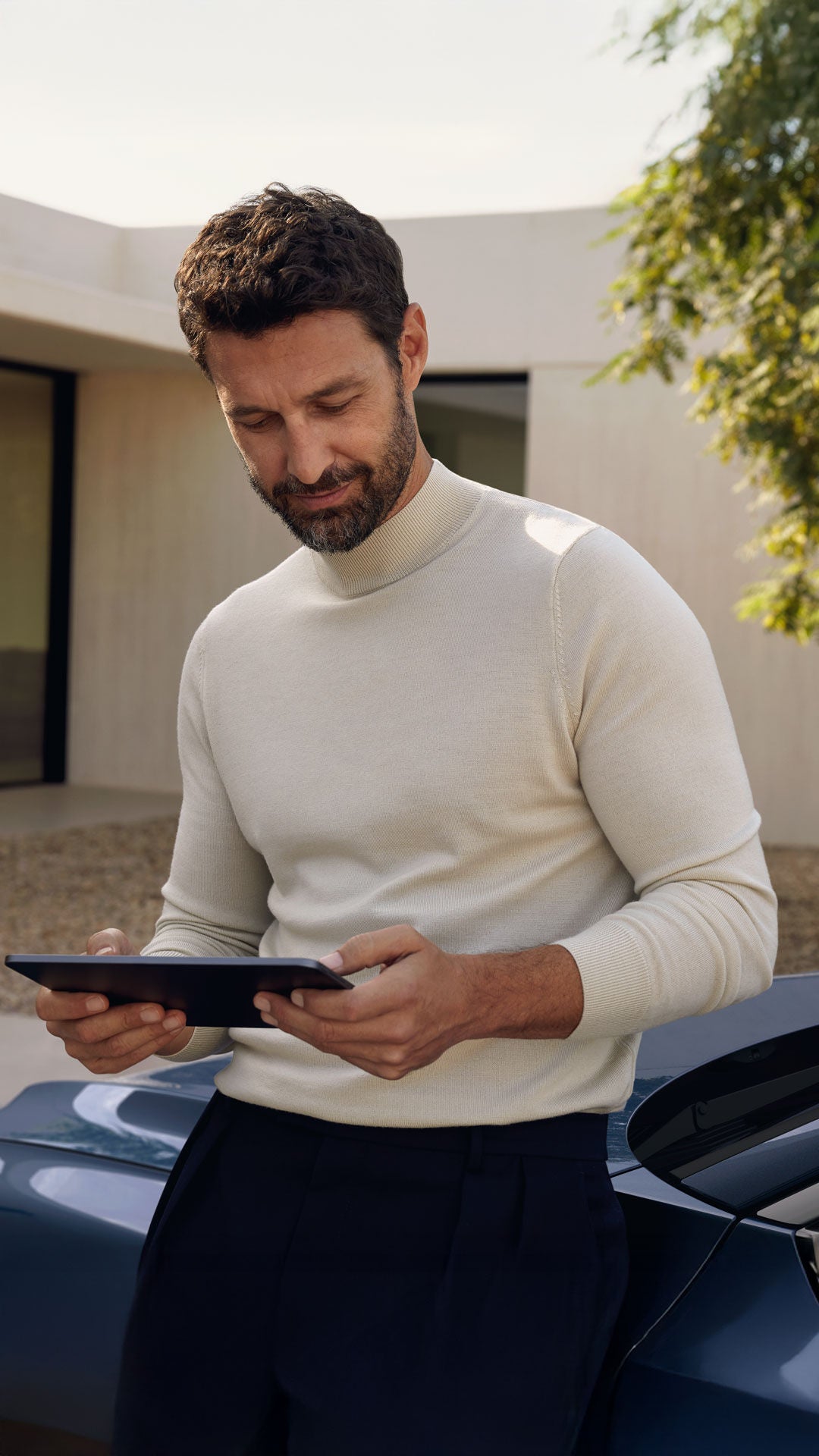 Mann sitzt auf der Fronthaube mit einem Tablet in der Hand