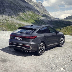 Schräge Heckansicht des SQ5 Sportback in der Edition One mit Akzenten in Magnesiumgrau. Im Hintergrund eine bergige Landschaft.