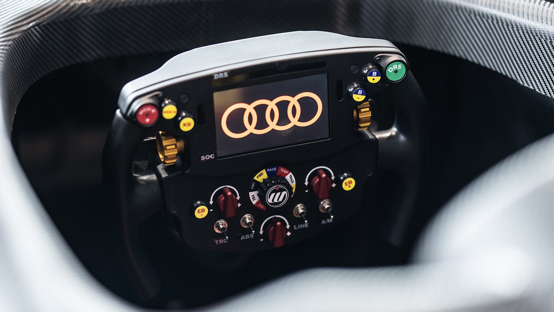 Nahaufnahme des Lenkrads im Audi racing Simulator mit Audi Ringen auf dem Display und farbigen Bedienelementen.