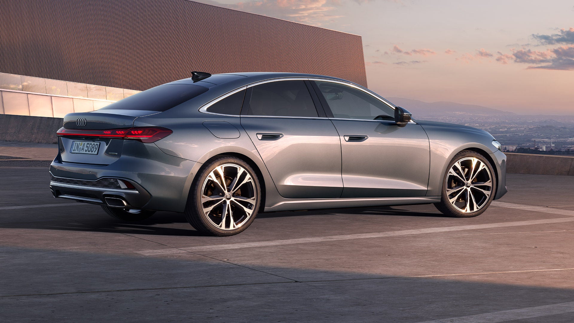 Seitenansicht einer silbernen Audi A5 Limousine vor moderner Architektur bei Sonnenuntergang.