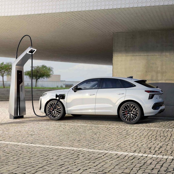 A white Q3 Sportback e-hybrid parked in front of an urban building is charging at a public charging station.