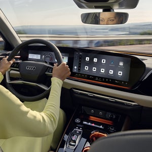 Blick von der Rückbank in das Cockpit der A5 Limousine. Eine Frau hält das Lenkrad in beiden Händen.