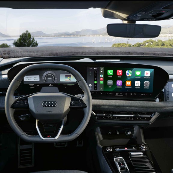 Vy från förarens perspektiv av ratten, med Audi virtual cockpit bakom och MMI touch-displayen i cockpiten på S6 Sportback e-tron. MMI touch-displayen visar Apple CarPlay-funktionen.