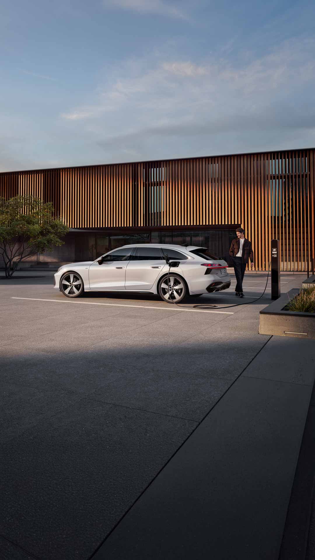 Audi A6 Avant e-hybrid står parkerad vid en laddstation. En person står bakom bilen.