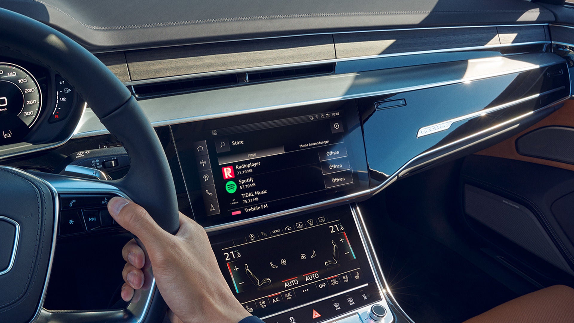 Hand am Audi-Lenkrad mit Blick auf das zentrale Infotainmentsystem mit Musik-Apps.
