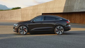 A black Audi vehicle parked on asphalt with a concrete wall in the background
