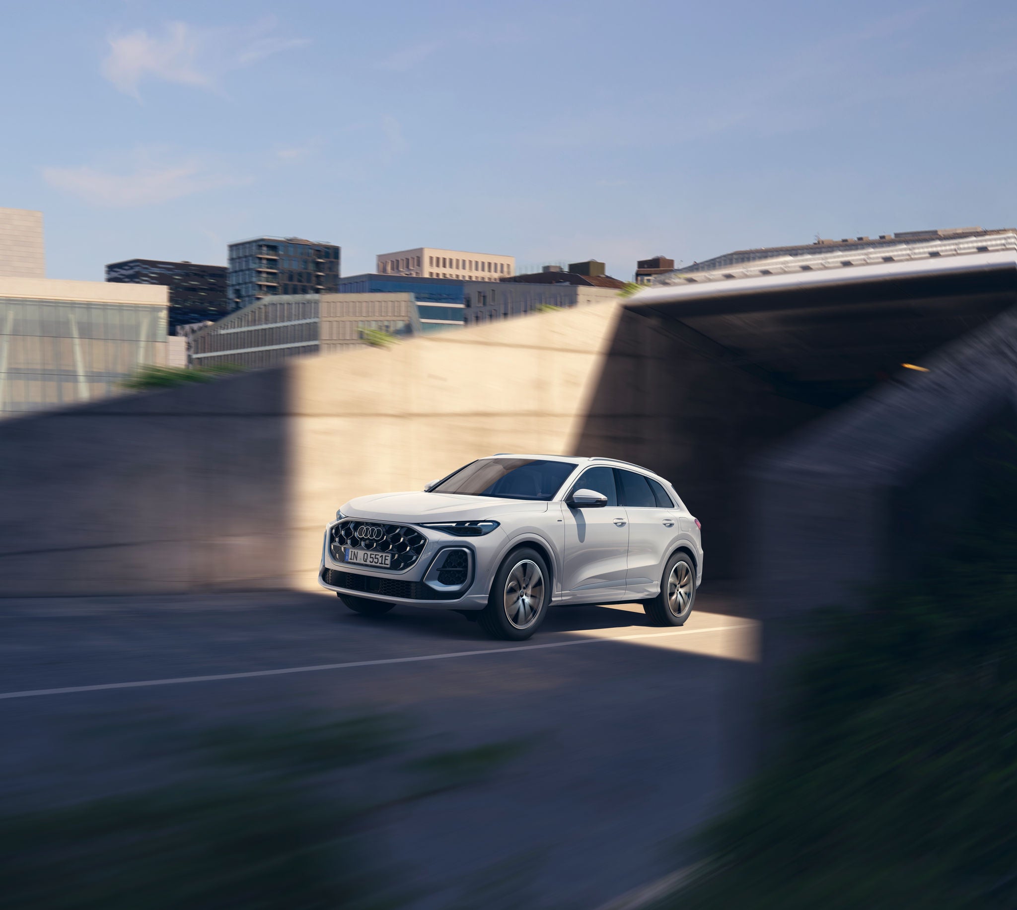 A white Audi Q5 SUV navigates a modern, shadowy urban environment, showcasing its stylish design and dynamic movement. 
