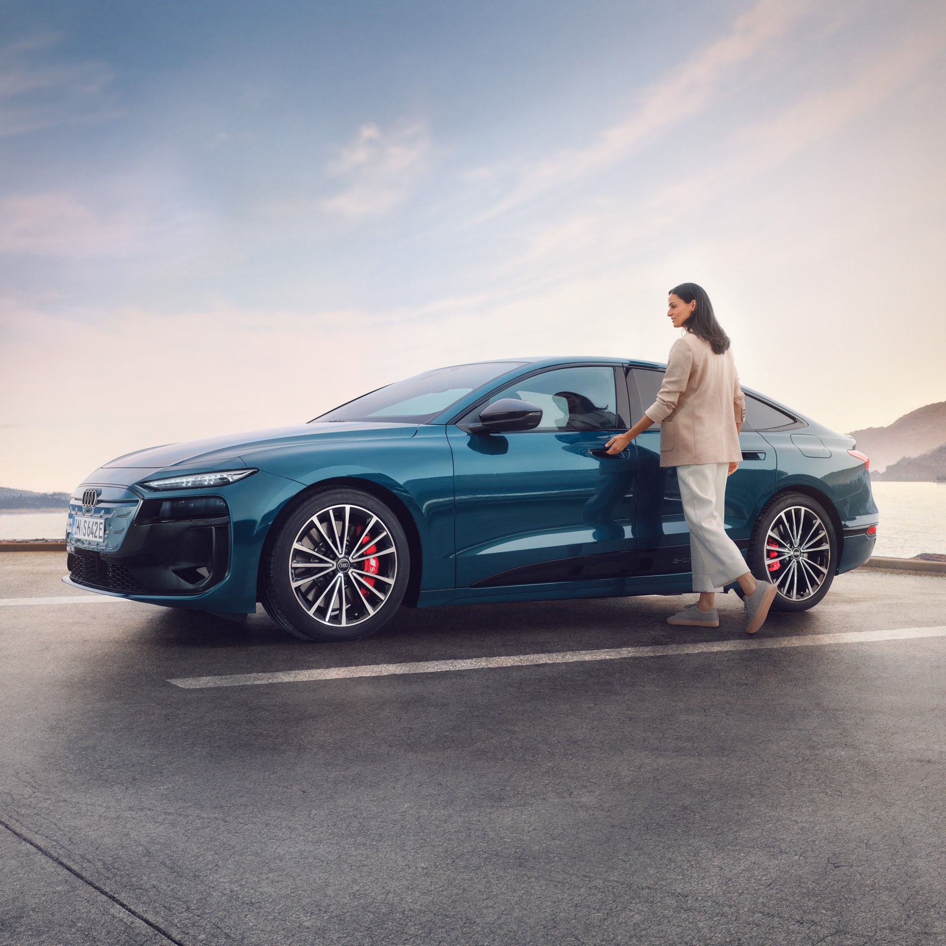 Eine Frau steht neben einem blauen Audi Modell und öffnet die Fahrertür bei weichem Abendlicht.