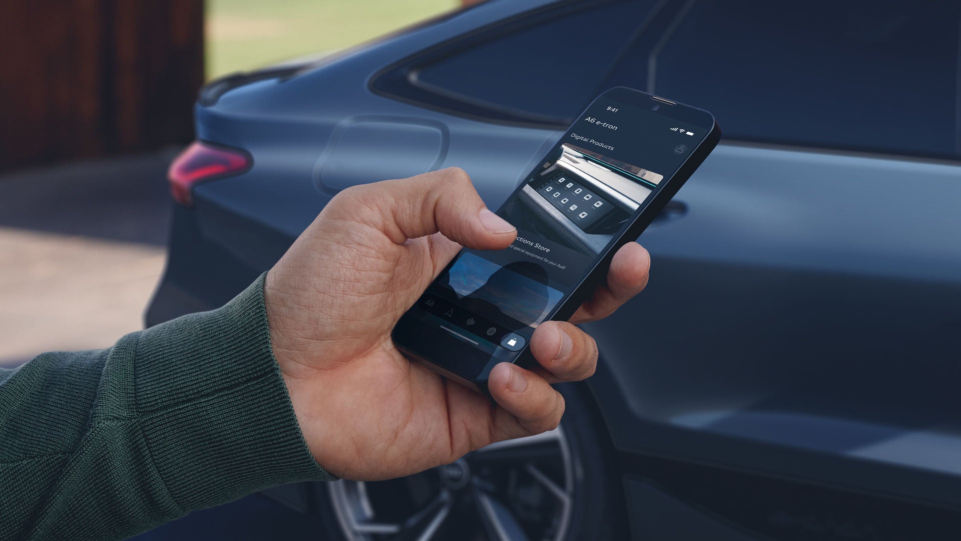 A man's hand protrudes into the picture from the left. He is holding a smartphone in his hand. A dark blue Audi A6 stands slightly out of focus in the background.