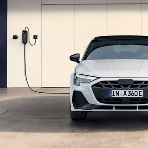 A sleek white Audi electric car is parked in front of a modern garage, plugged into a wall-mounted charging station, conveying innovation and sustainability.