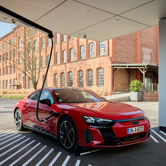 Ein roter Audi A6 e-tron wird an einer Ladesäule vor einem Backsteingebäude geladen.