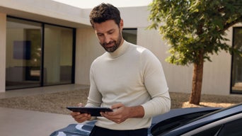 Mann sitzt auf der Fronthaube mit einem Tablet in der Hand