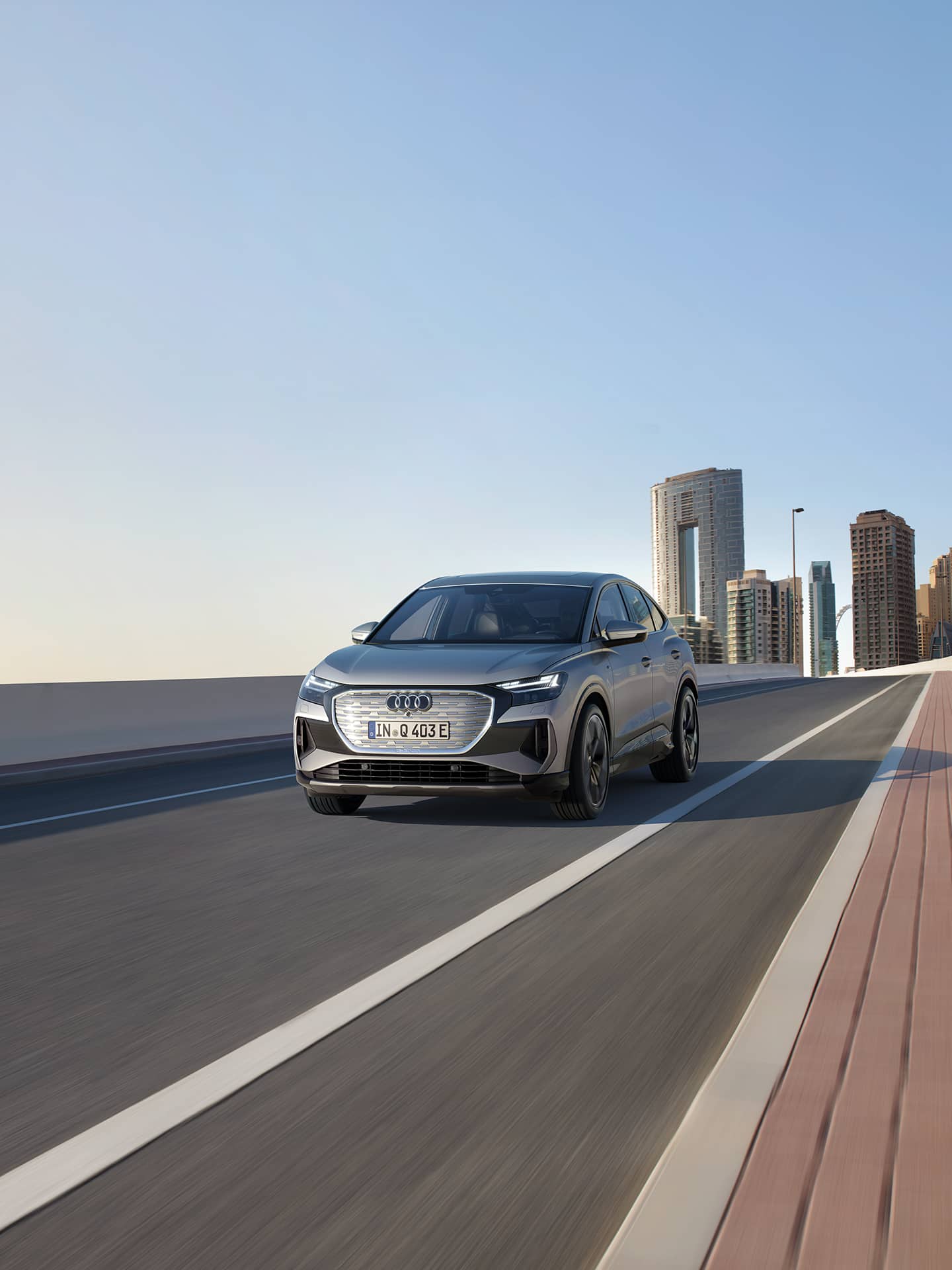 Silberner Audi Q4 Sportback e-tron fährt auf einer modernen Stadtbrücke, im Hintergrund Hochhäuser unter blauem Himmel.