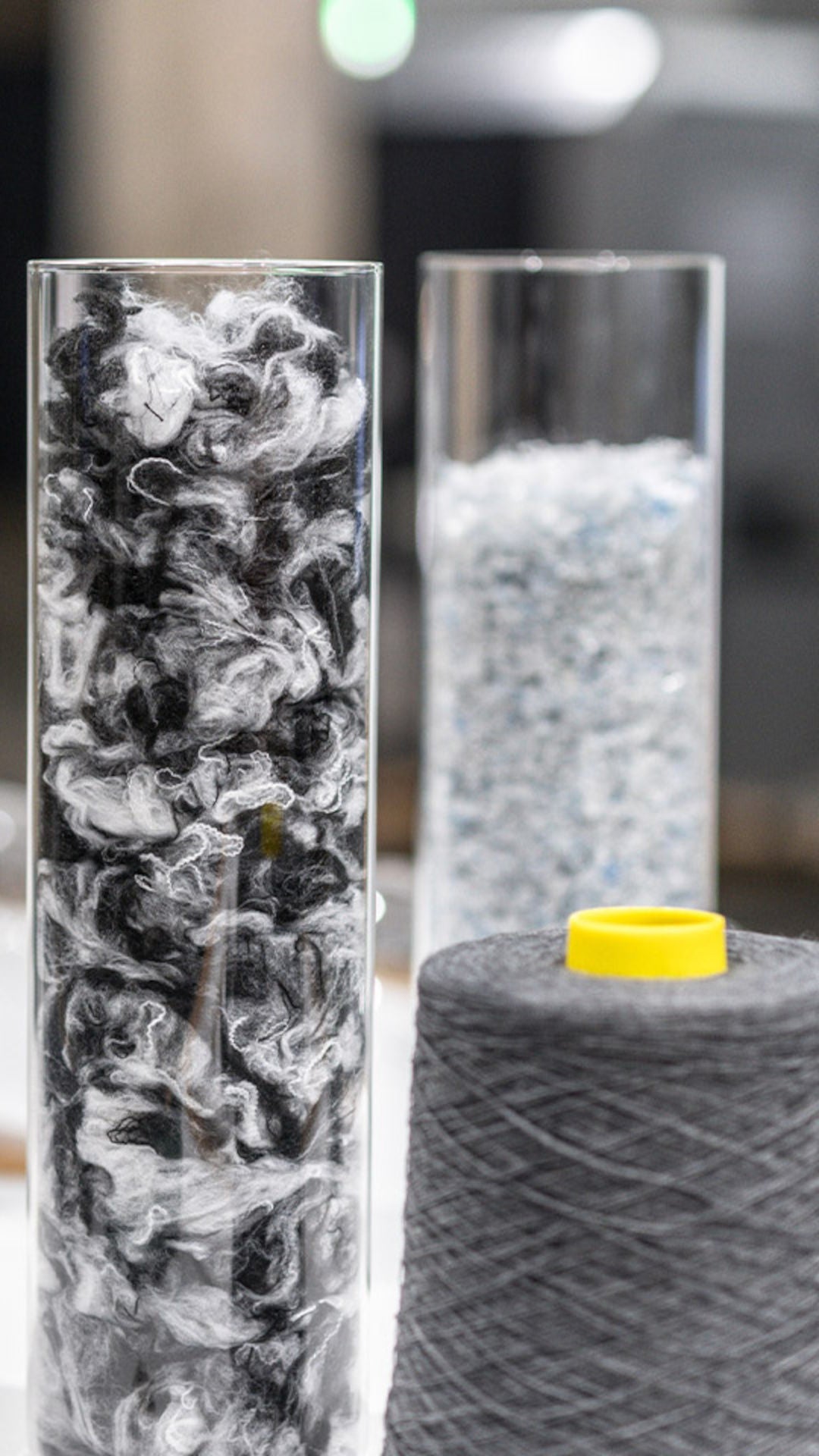 Several glass cylinders containing fibers and granules and a gray spool of thread on a table