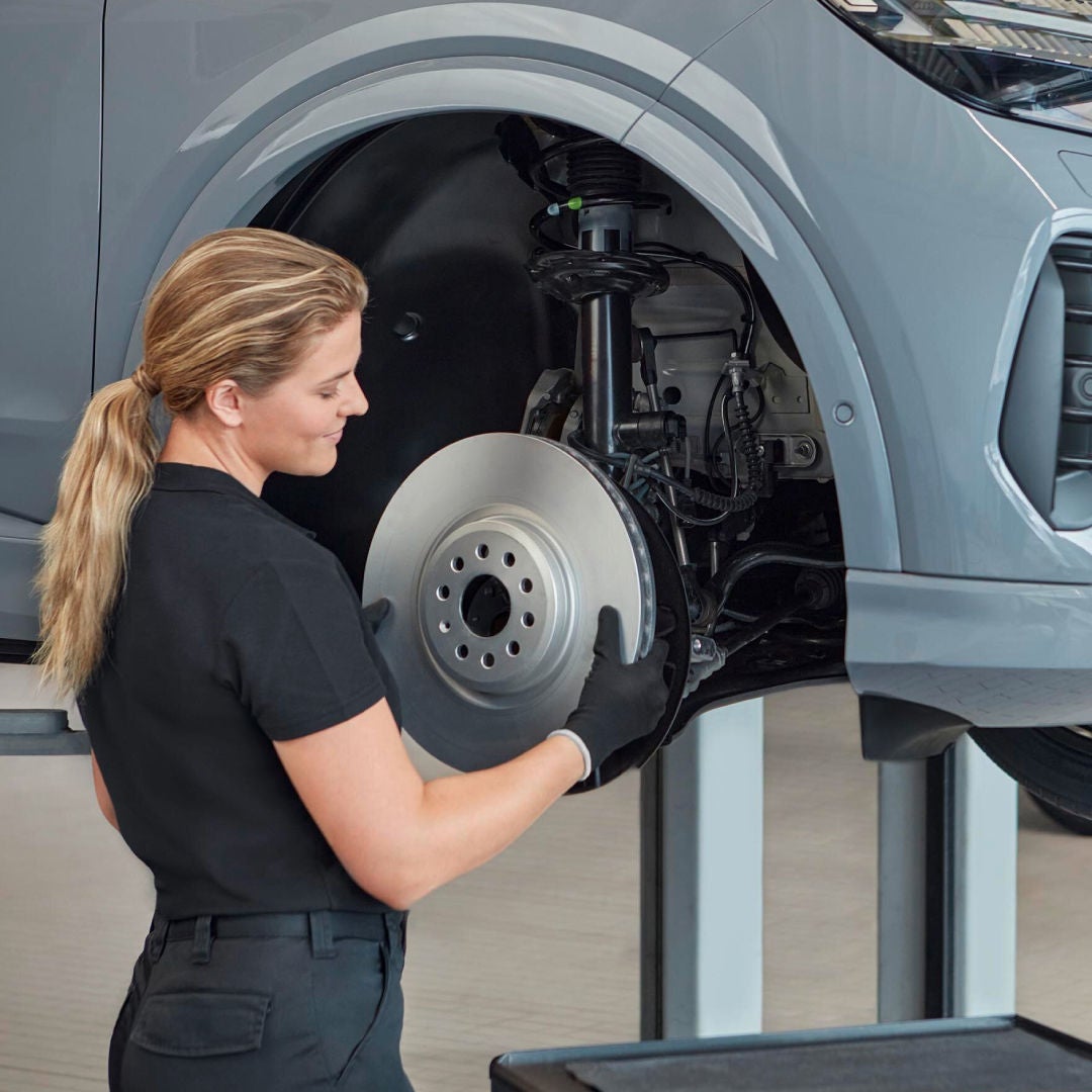 Un'addetta all'officina sta installando un disco freno nuovo su un'auto Audi.