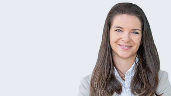 Dr. Samantha Maria Mayinger: Porträt einer jungen, lächelnden Frau mit brünettem langen Haar auf grauem Hintergrund.