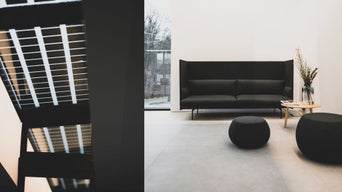 Moderner Wartebereich mit schwarzem Sofa, zwei runden Hockern und einem Beistelltisch mit Vase und Zeitschriften.