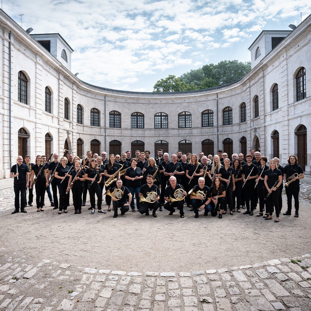 Großes Blasorchester in schwarzer Kleidung mit Instrumenten im Innenhof eines historischen Gebäudes.