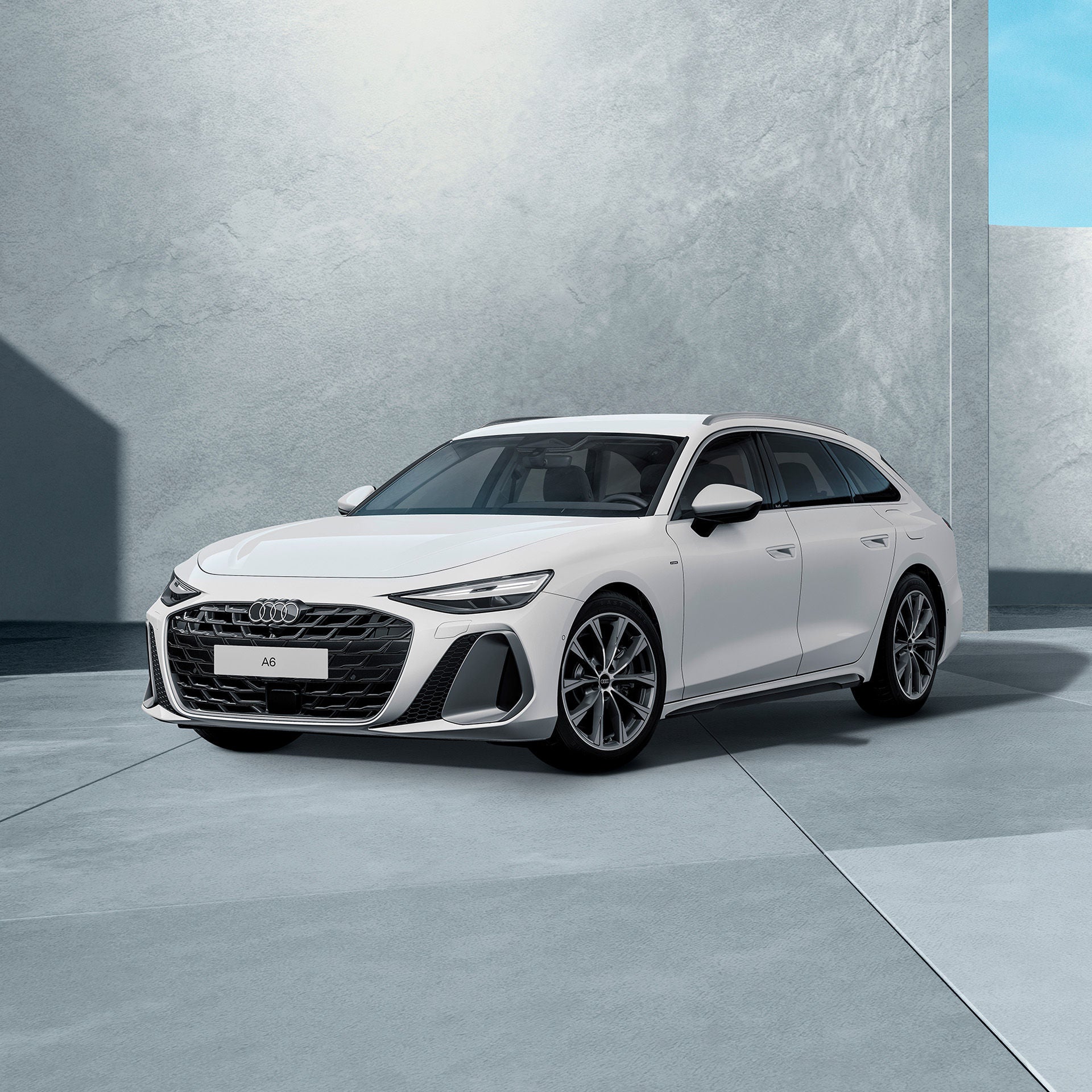 Ein weißer Audi A6 Avant e-hybrid von schräg vorne fotografiert vor einer modernen Kulisse.