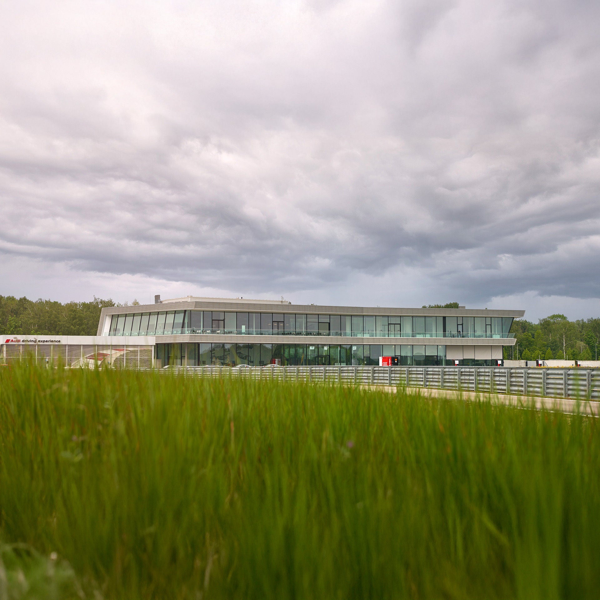 Blick über eine grüne Wiese auf die Rennstrecke Neuburg. Im Hintergrund ist das Gebäude des Audi driving centers zu sehen.