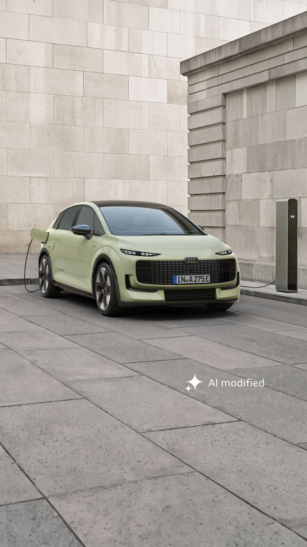 The Audi A2 e-tron, photographed from the front and from behind, is parked in front of a modern building. The car is connected to a charging point.