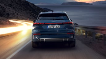 Der e-tron GT quattro fährt bei Sonnenuntergang über eine kurvige Straße entlang einer felsigen Küste.