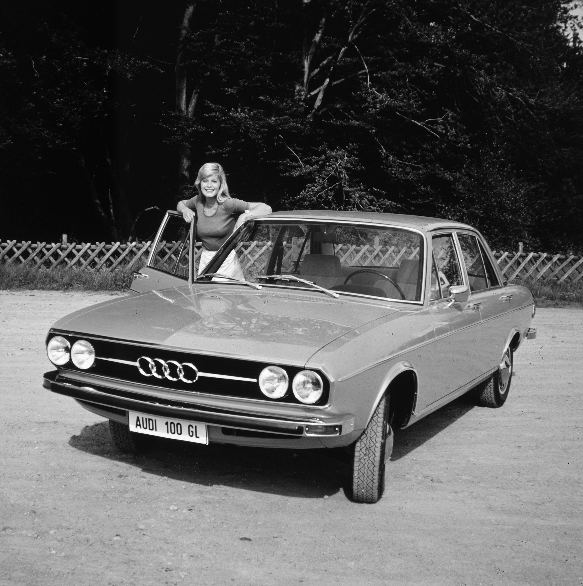 En svartvit bild på Audi 100 GL. En kvinna står vid passagerardörren.