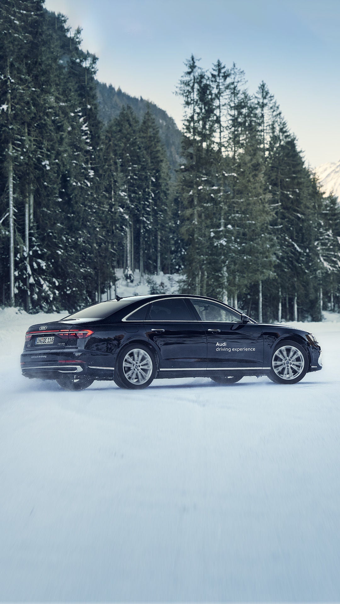 Schwarzer Audi Audi A8 50 TDI quattro fährt im Schnee, im Hintergrund sind Wälder.