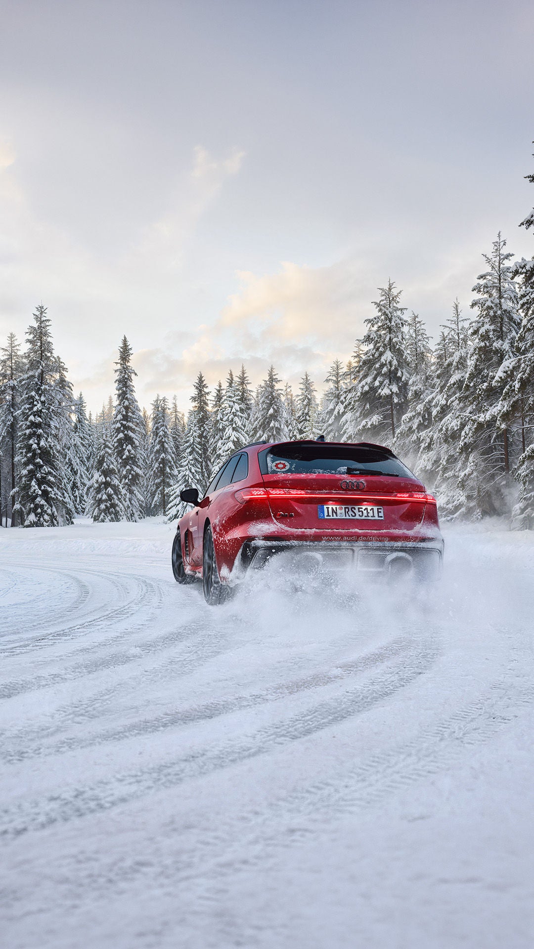 Rear view of a red Audi RS 5 Avant on a snow-covered road; swirling snow, tire tracks, and a forest.