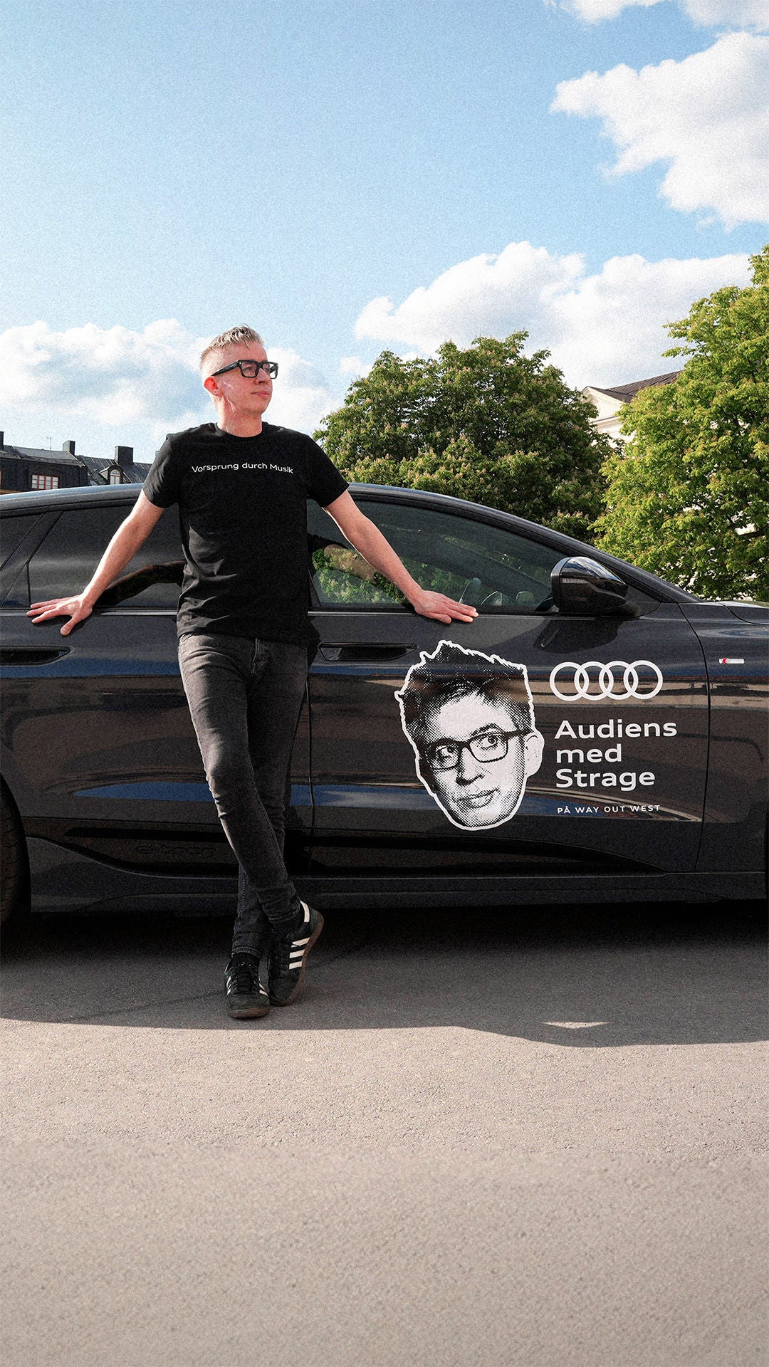 Fredrik Strage lutad mot en mörk Audi A6 e-tron med logotypen för Audiens med Strage