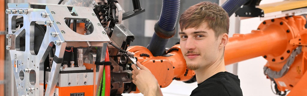 Auszubildender arbeitet an einer Maschine und schaut in die Kamera
