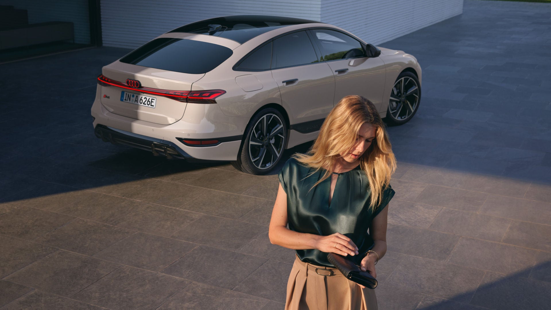 A woman looking at her phone while she is a few meters away from a white Audi e-tron car