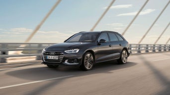 Schwarzer Audi A4 Avant fährt auf einer Brücke bei Tageslicht, im Hintergrund Himmel mit leichten Wolken und Brückenseile.